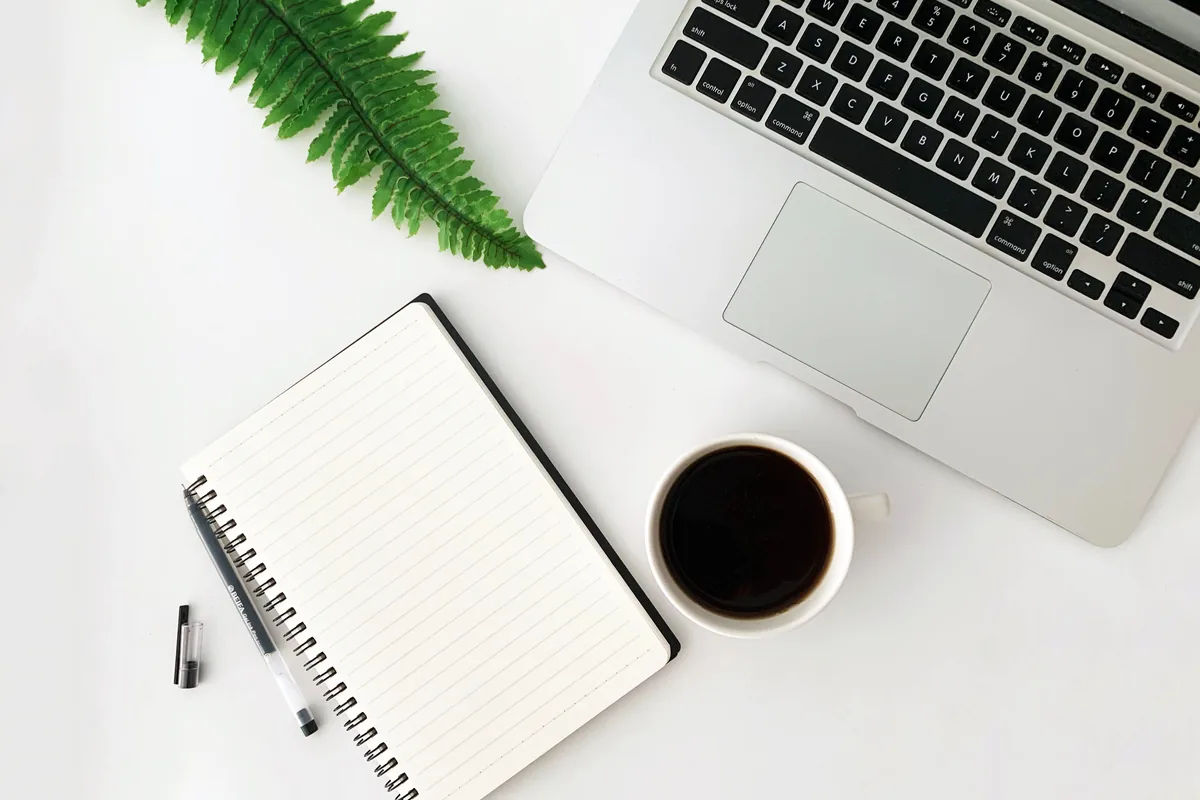 Laptop, blank notebook and a cup of coffee on a clean white desk