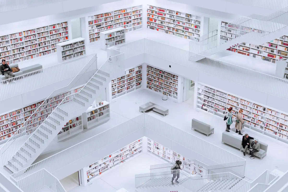 Bright white library atrium with tiers of shelves and stairs, and readers moving between the levels