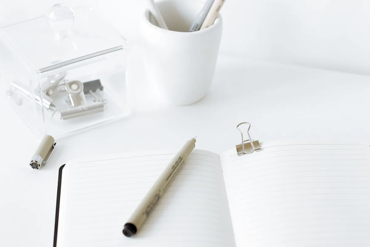 Open notebook and pen on a white desk with stationery