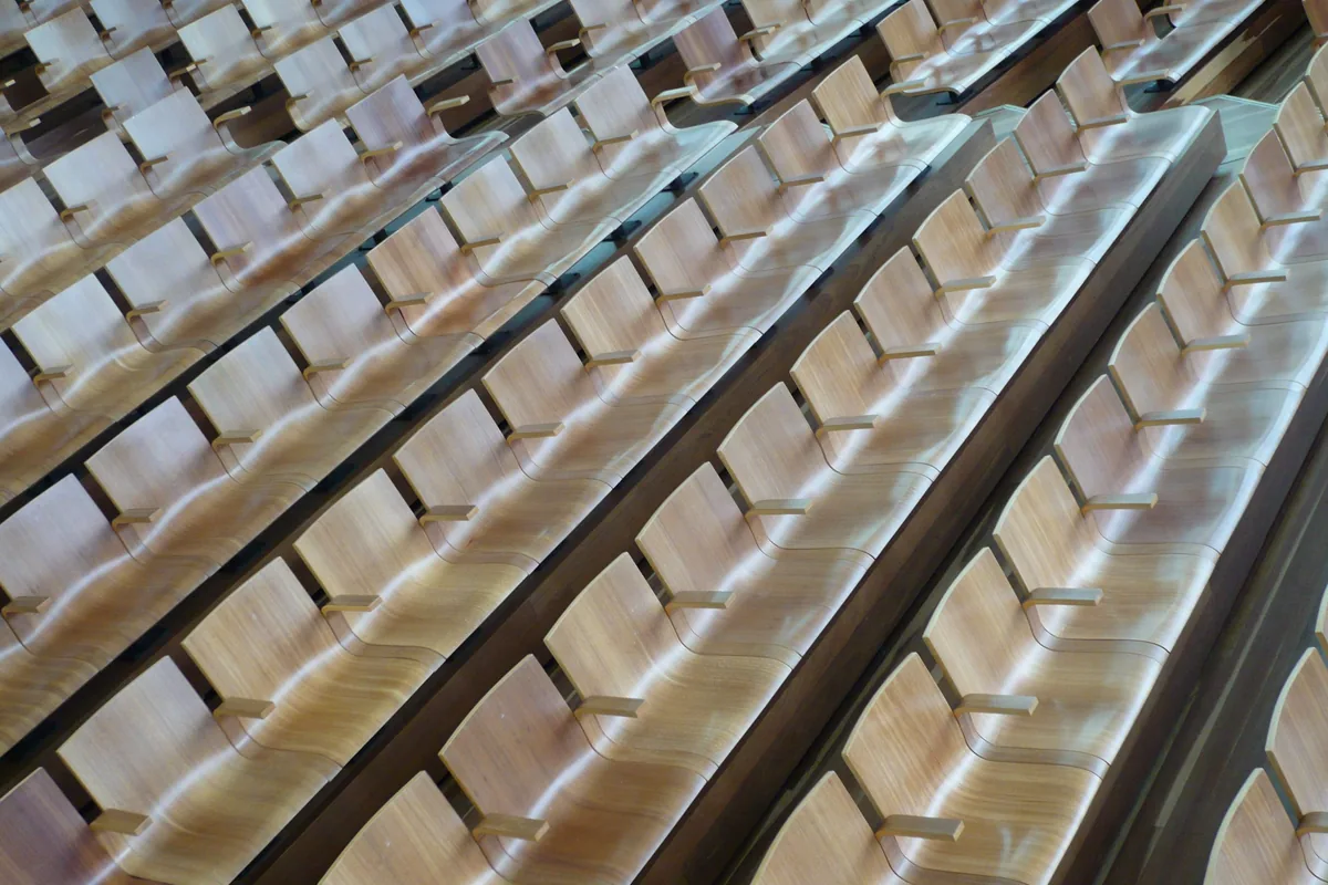 Rows of curved wooden seats in a lecture theatre, seen at an angle
