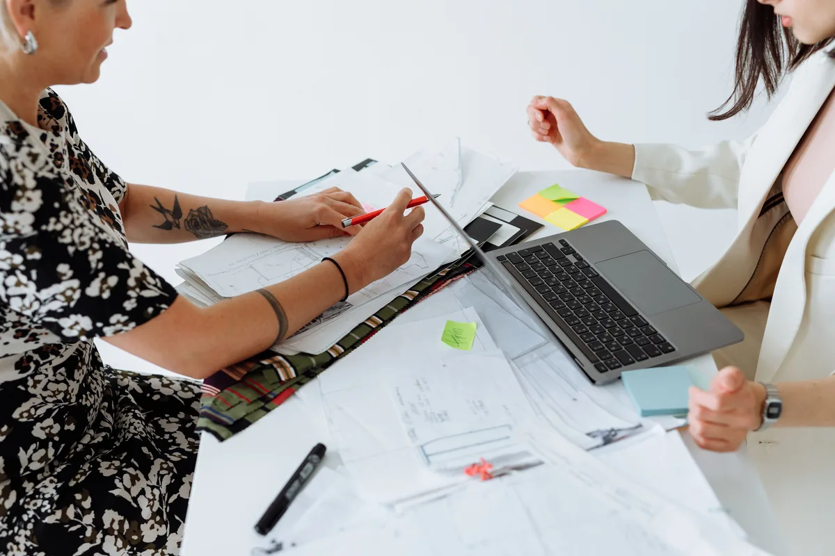 Two people working through printed documents, notes and a laptop on a white desk