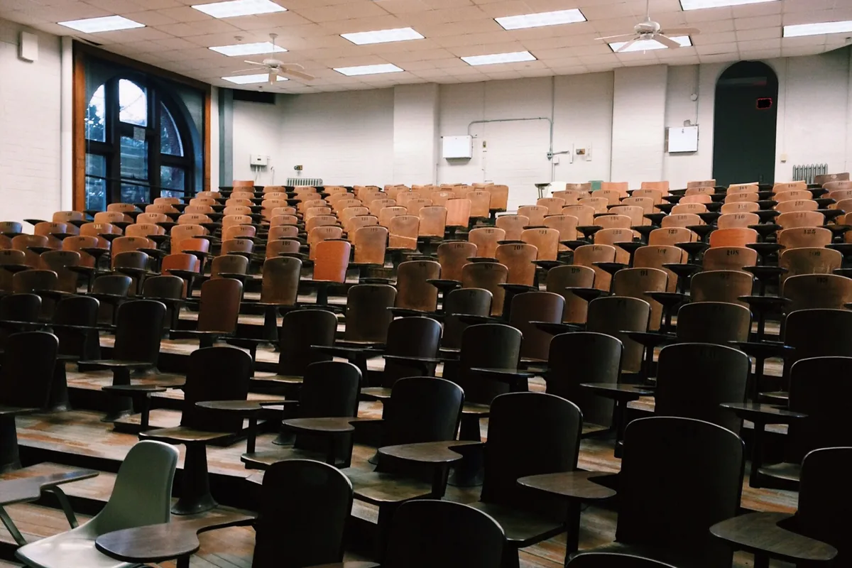 Rows of empty dark seats with fold-down desks in a large lecture auditorium