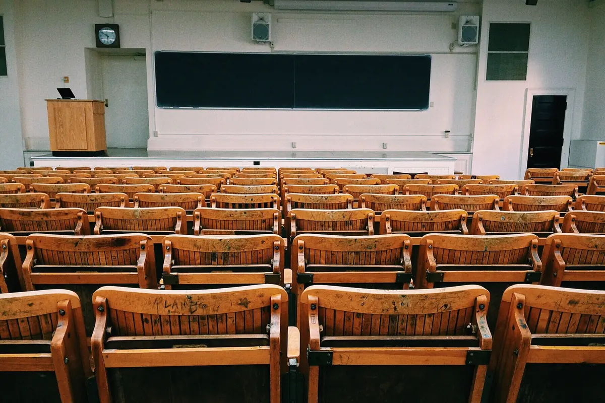 Empty lecture hall with rows of wooden seats facing a blackboard and lectern