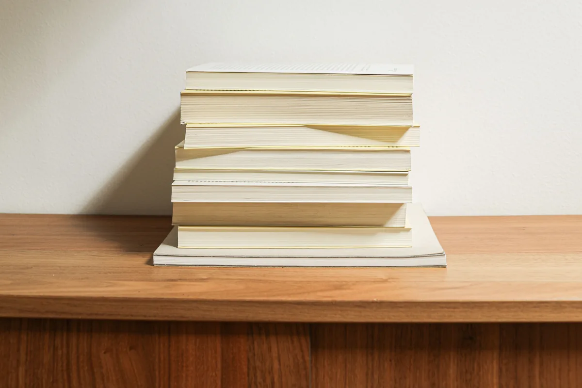 Stack of books on a wooden desk against a plain wall