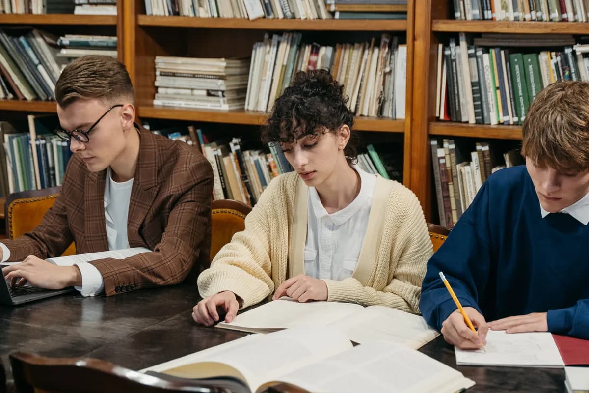 Three students studying together at a library table in front of bookshelves