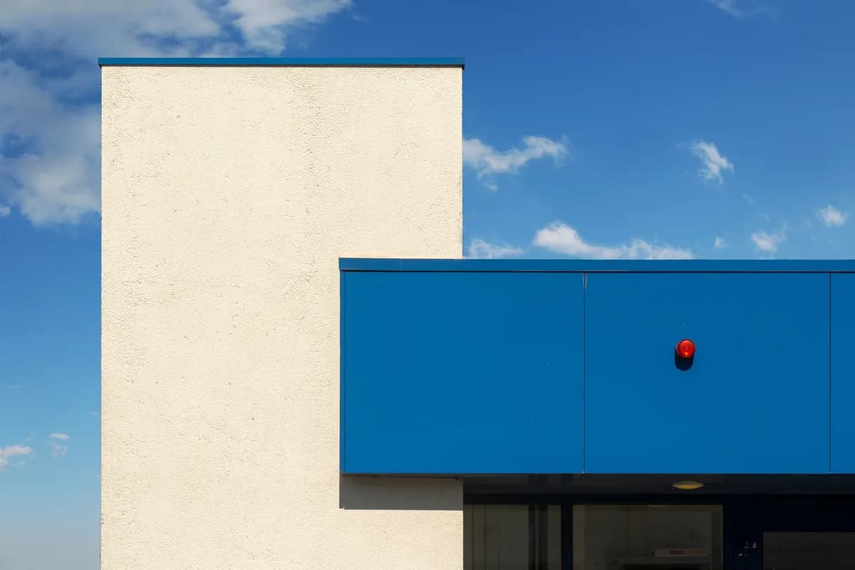 Minimalist white and blue building facade under a blue sky with light cloud